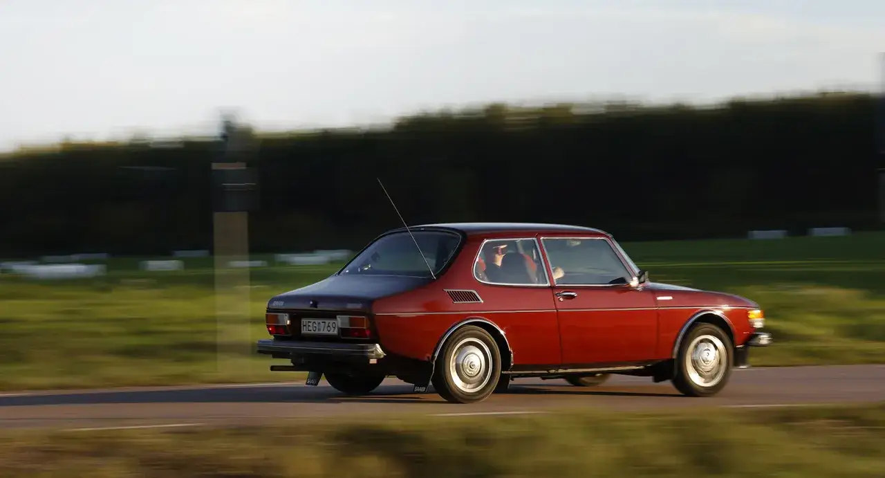 R&ouml;d Saab 99 EMS k&ouml;r l&auml;ngs en landsv&auml;g i solnedg&aring;ngen.