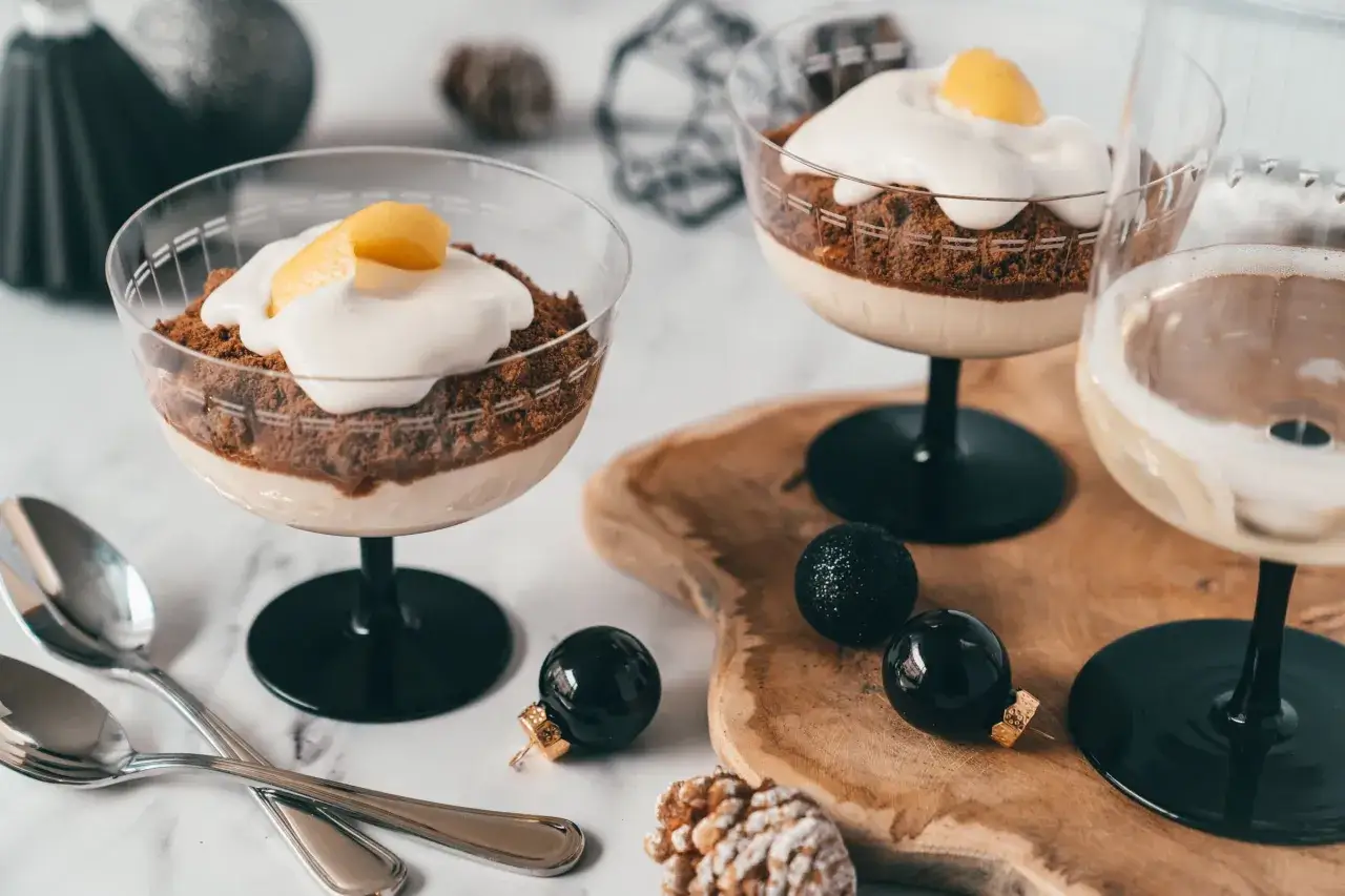 Zwei Schokoladen-Desserts mit Sahne und Zitrone, daneben ein Glas süßer Champagner und Weihnachtskugeln.