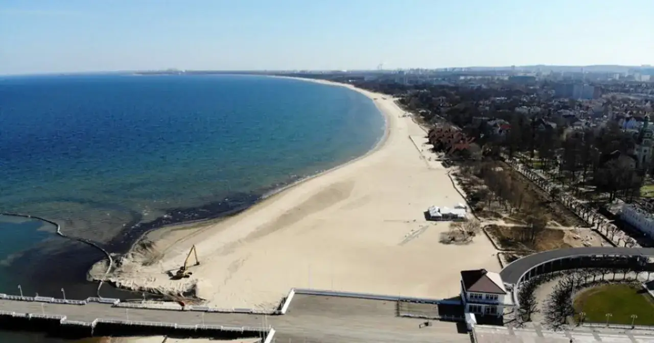 Sopot co warto zobaczyć: szeroka plaża, molo i zabudowania nadmorskie. W oddali widać panoramę miasta.