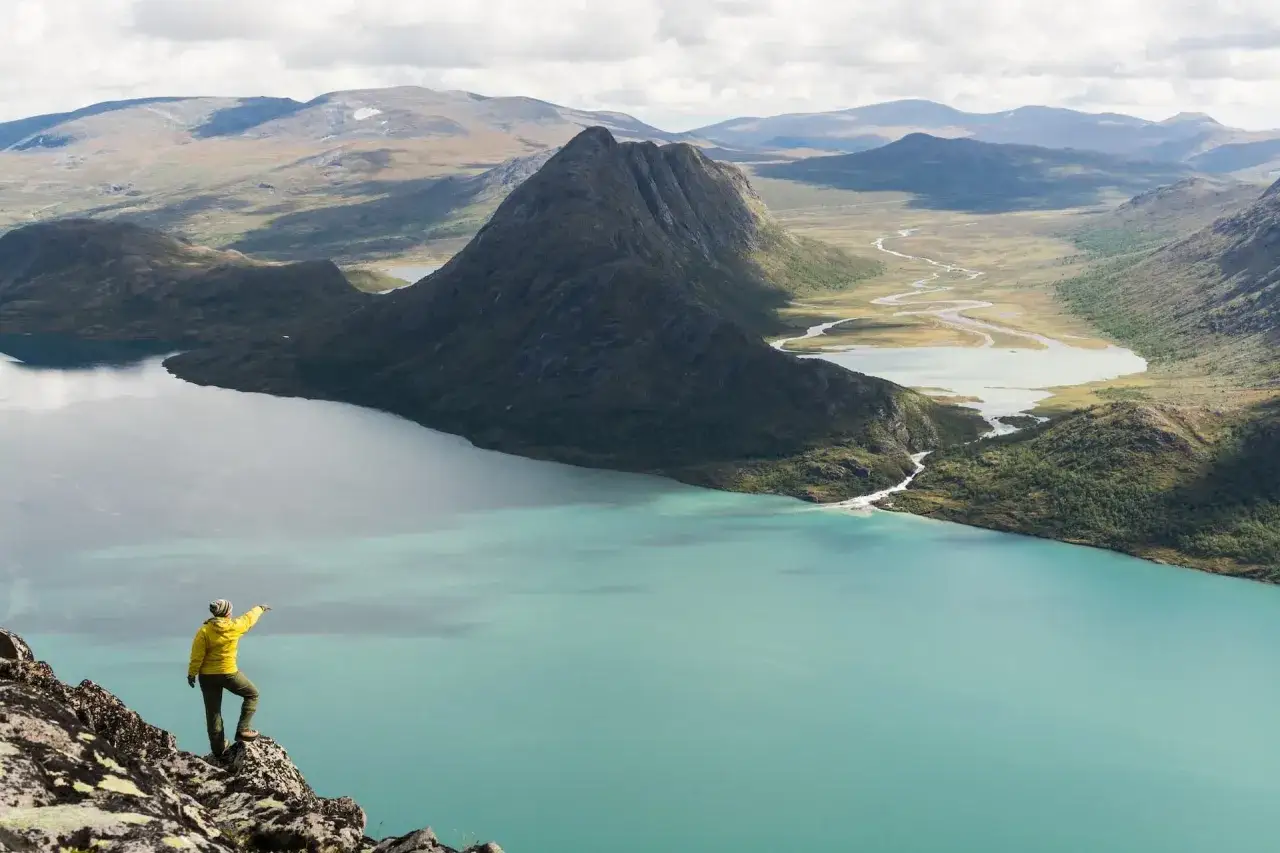 Vandrare pekar mot en turkos sj&ouml; och berg. Besseggen sv&aring;righetsgrad &auml;r utmanande men bel&ouml;nande.