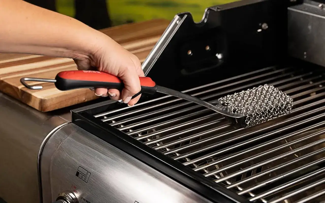 En hand använder en grillborste för att rengöra gasolgrillens galler.