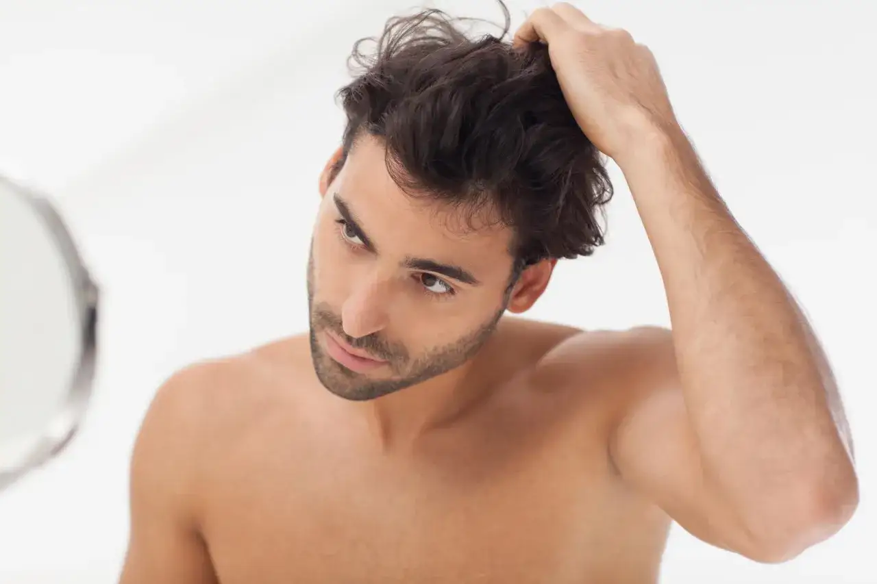 Hombre revisando su cabello en el espejo, parte de su rutina de cuidado del cabello hombre.