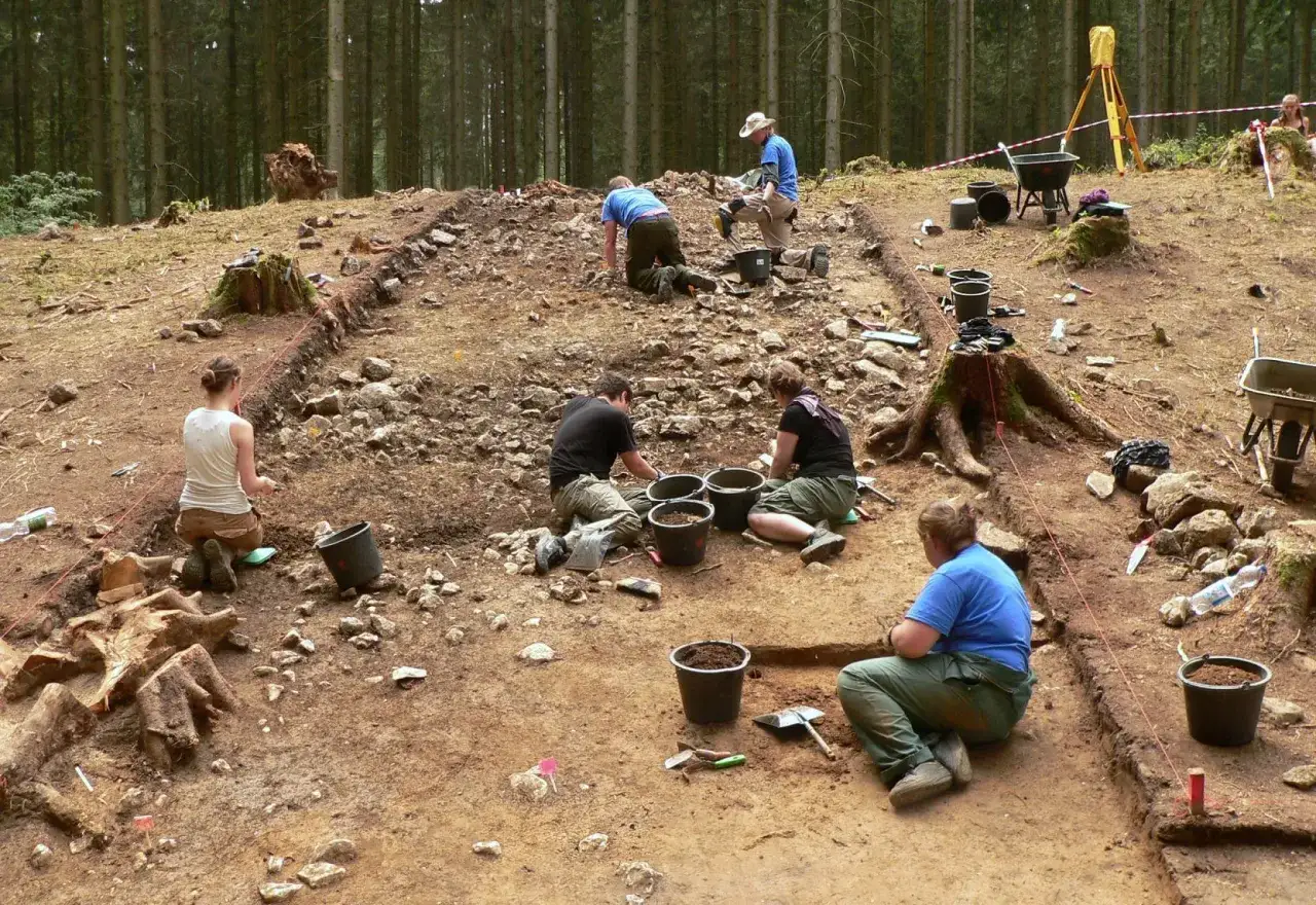 Archeologowie pracują w lesie, odsłaniając ślady przeszłości. Wszyscy skupieni na swoich zadaniach.