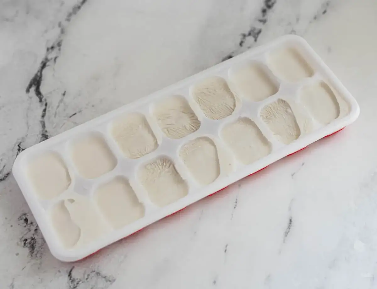 Eiswürfelform mit Kokosmilch, bereit zum Kokosmilch einfrieren. Einige Würfel sind bereits gefroren, andere noch flüssig.