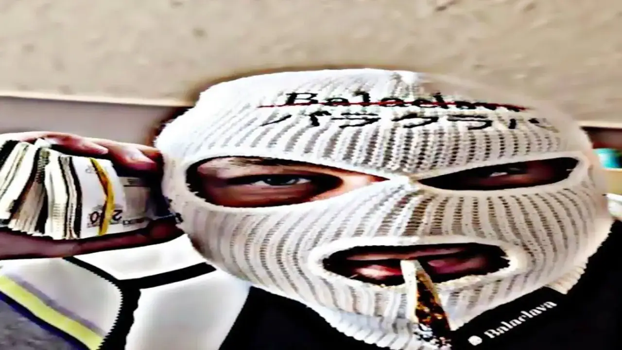 Osoba w masce balaclava trzyma plik banknot&oacute;w. Widać jej oczy i usta, przez kt&oacute;re przechodzi papieros.
