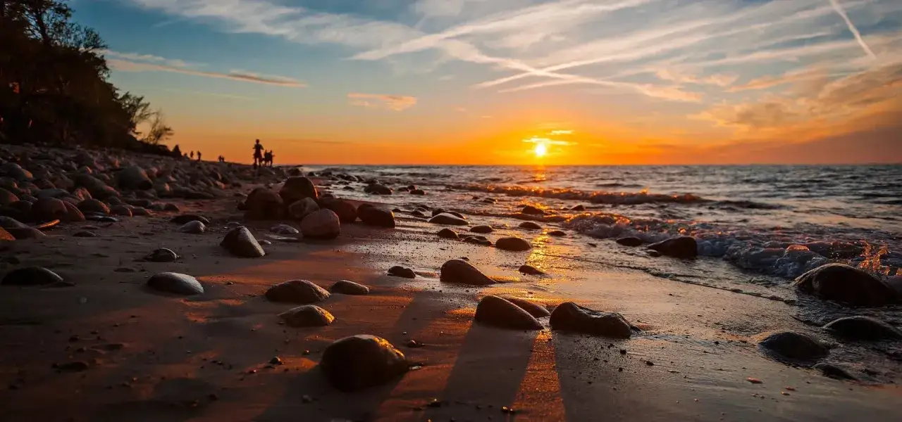 Zachód słońca w Jarosławcu. Kamienista plaża, fale obmywają brzeg, a niebo mieni się odcieniami pomarańczy i błękitu.