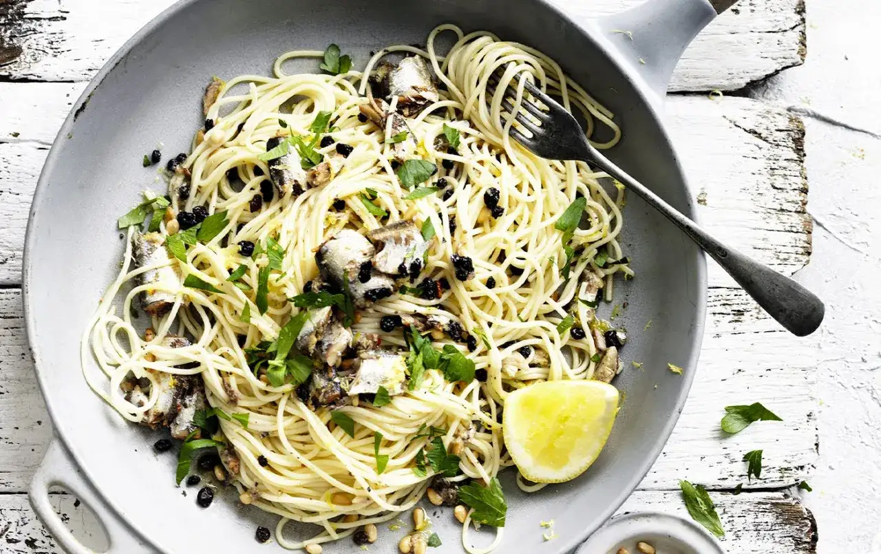 Un plat de p&acirc;tes aux sardines, garni de persil frais, de pignons de pin et d'une tranche de citron. Un d&eacute;lice simple et savoureux.