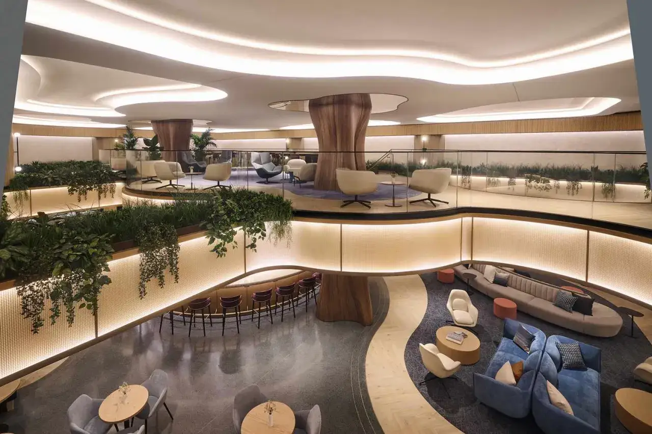 Moderne, begrünte Airport Lounge mit geschwungenen Deckenlichtern, bequemen Sitzbereichen und einem zentralen Baumstamm-Design.