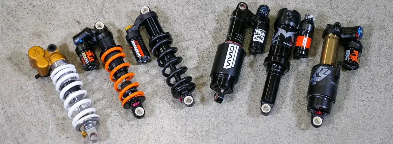 A lineup of bicycle rear shocks, showcasing both coil vs air shock designs from brands like Fox, RockShox, and Marzocchi.