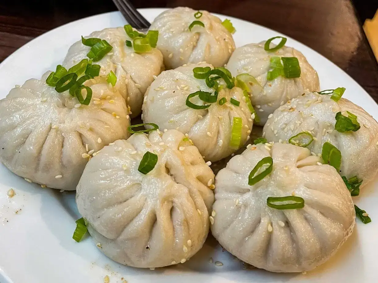 Pierożki baozi, delikatnie posypane sezamem i szczypiorkiem, czekają na talerzu.