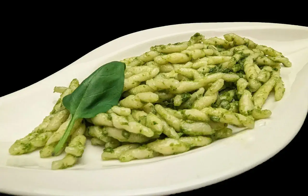 Trofie al pesto, une recette italienne authentique, servie sur une assiette blanche avec une feuille de basilic frais.