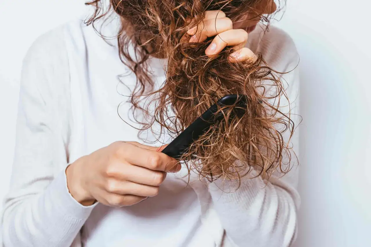 Une personne peigne ses cheveux mouillés, qui sont visiblement emmêlés à la racine.