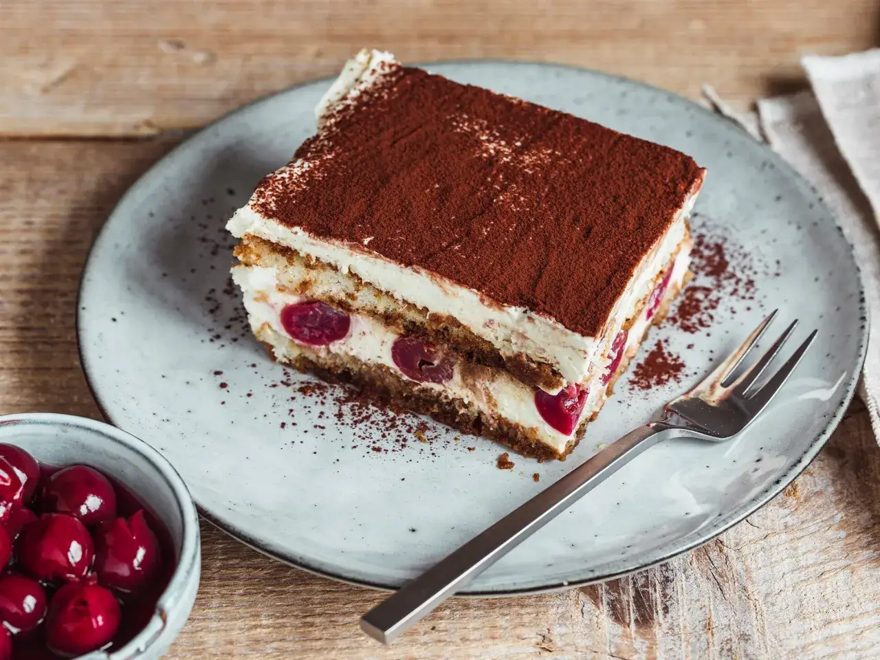 Ein St&uuml;ck Kirsch-Tiramisu, verfeinert mit Kakaopulver. Perfekt f&uuml;r alle, die nach neuen Tiramisu Rezepte suchen.