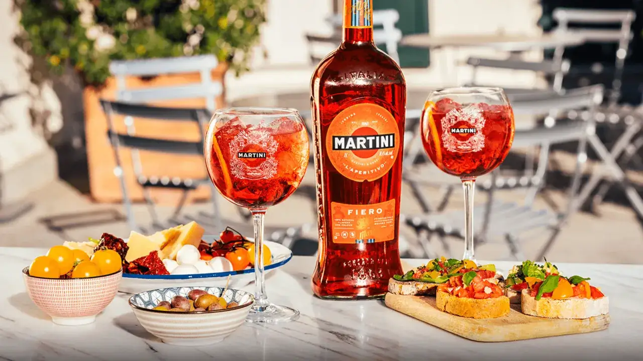 Let's raise a glass! Dwa drinki z Martini Fiero, butelka Martini Fiero i przekąski na stole. Idealny aperitivo.