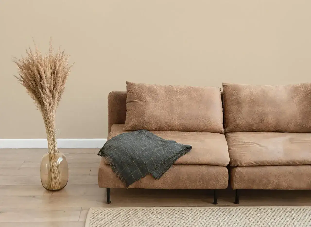 Gemütliche braune Couch mit karierter Decke vor heller Wand. Perfekt, um die Wandfarbe cosy zu kombinieren.