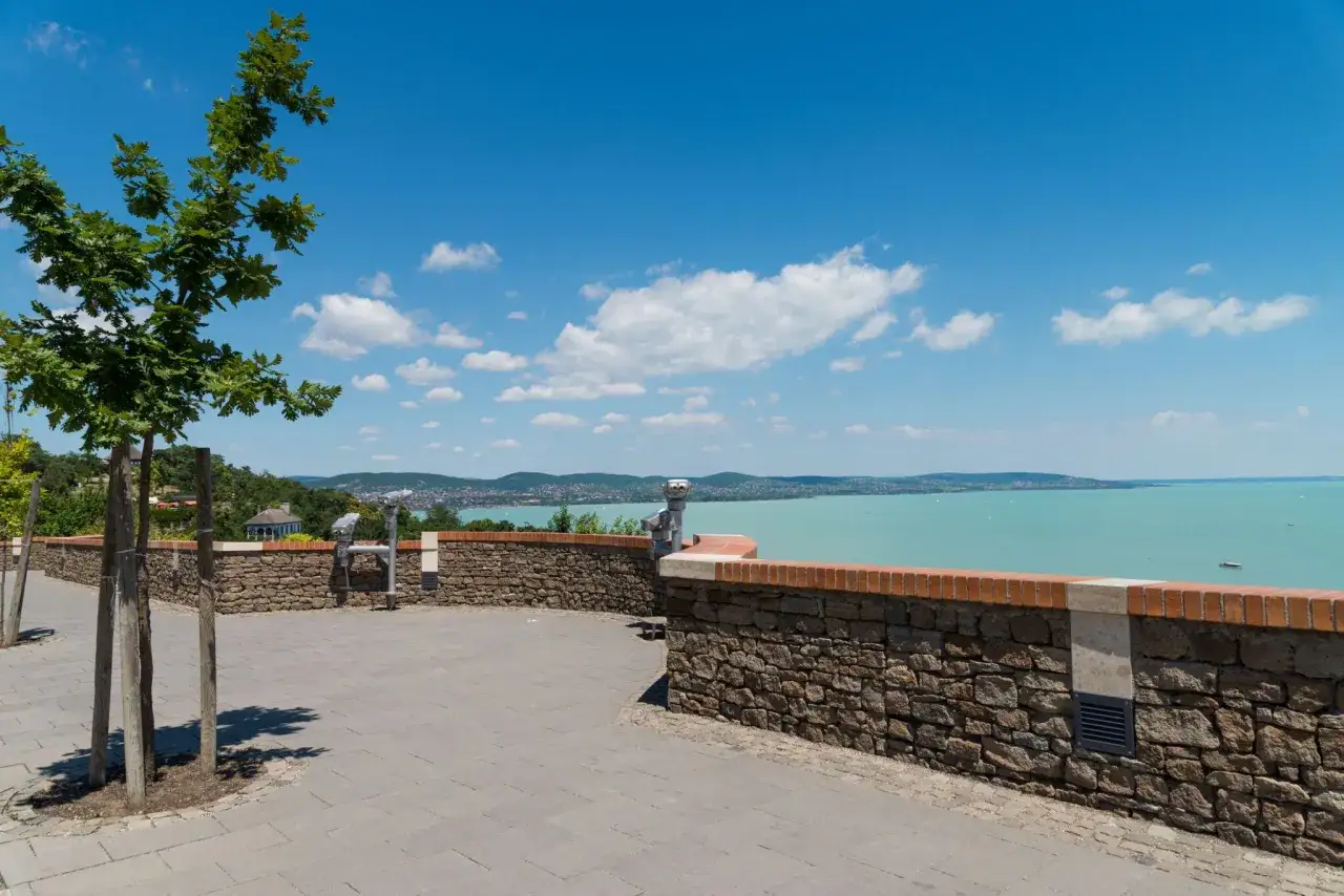 Widok na turkusowe wody Balatonu i malownicze miejscowości nad Balatonem. Widoczne lunety widokowe i kamienny murek.