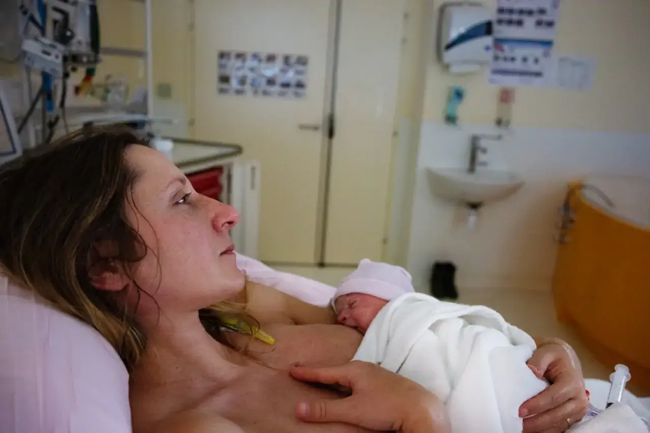 Po 39 tygodniu ciąży, mama tuli noworodka na piersi w szpitalnej sali.