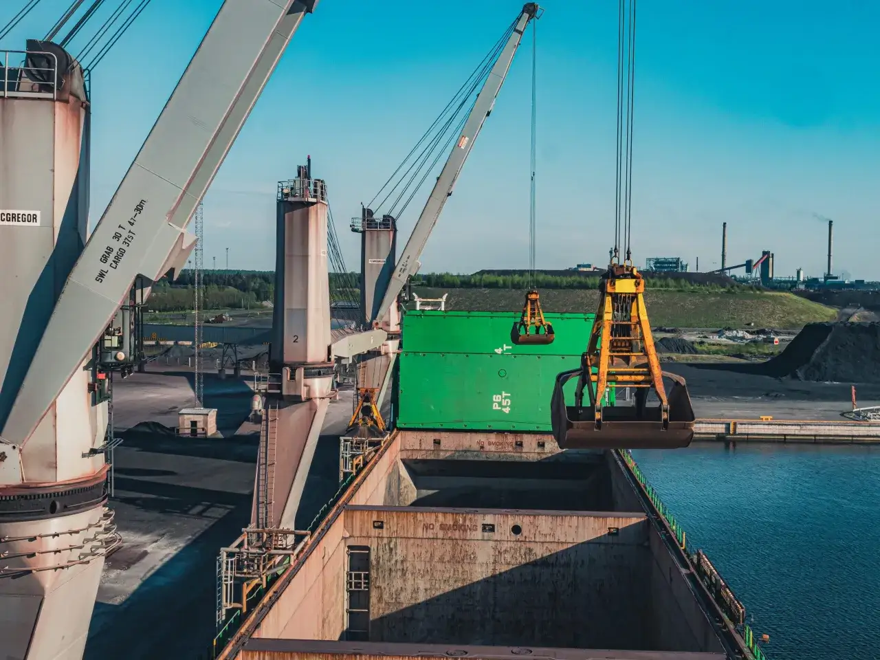 Dźwig portowy Cargotec rozładowuje zielony kontener z masowca.