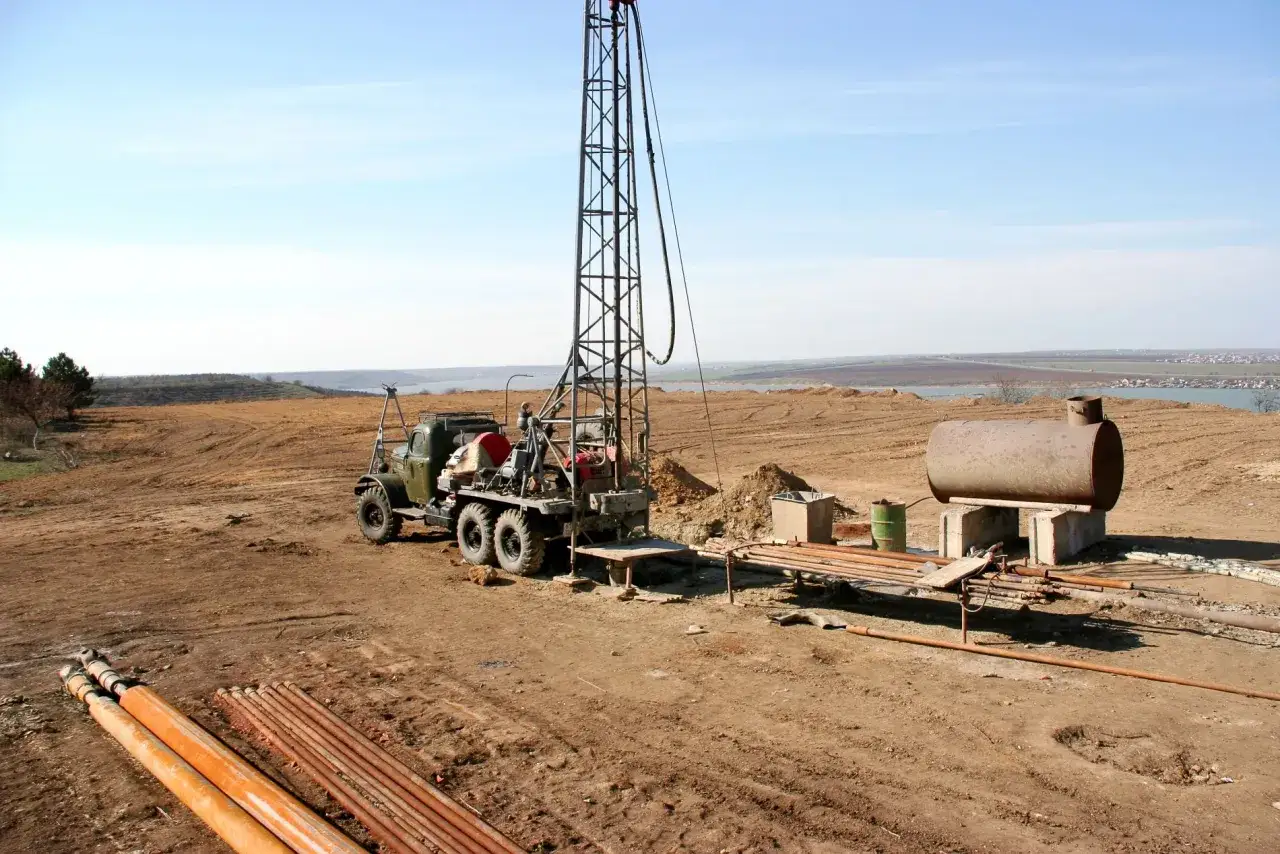 Attrezzatura per perforazione in un cantiere, pronta per scoprire come trovare l'acqua per fare un pozzo. Tubi e serbatoio in vista.