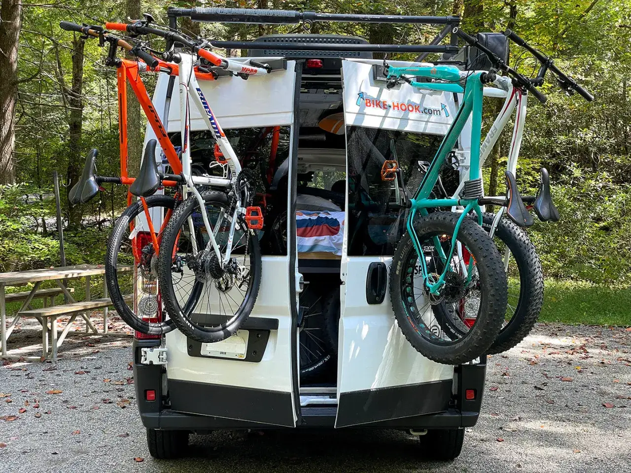 Comment fixer vélo dans soute camping car : deux vélos, un orange et un turquoise, sont accrochés à l'arrière d'un camping-car.