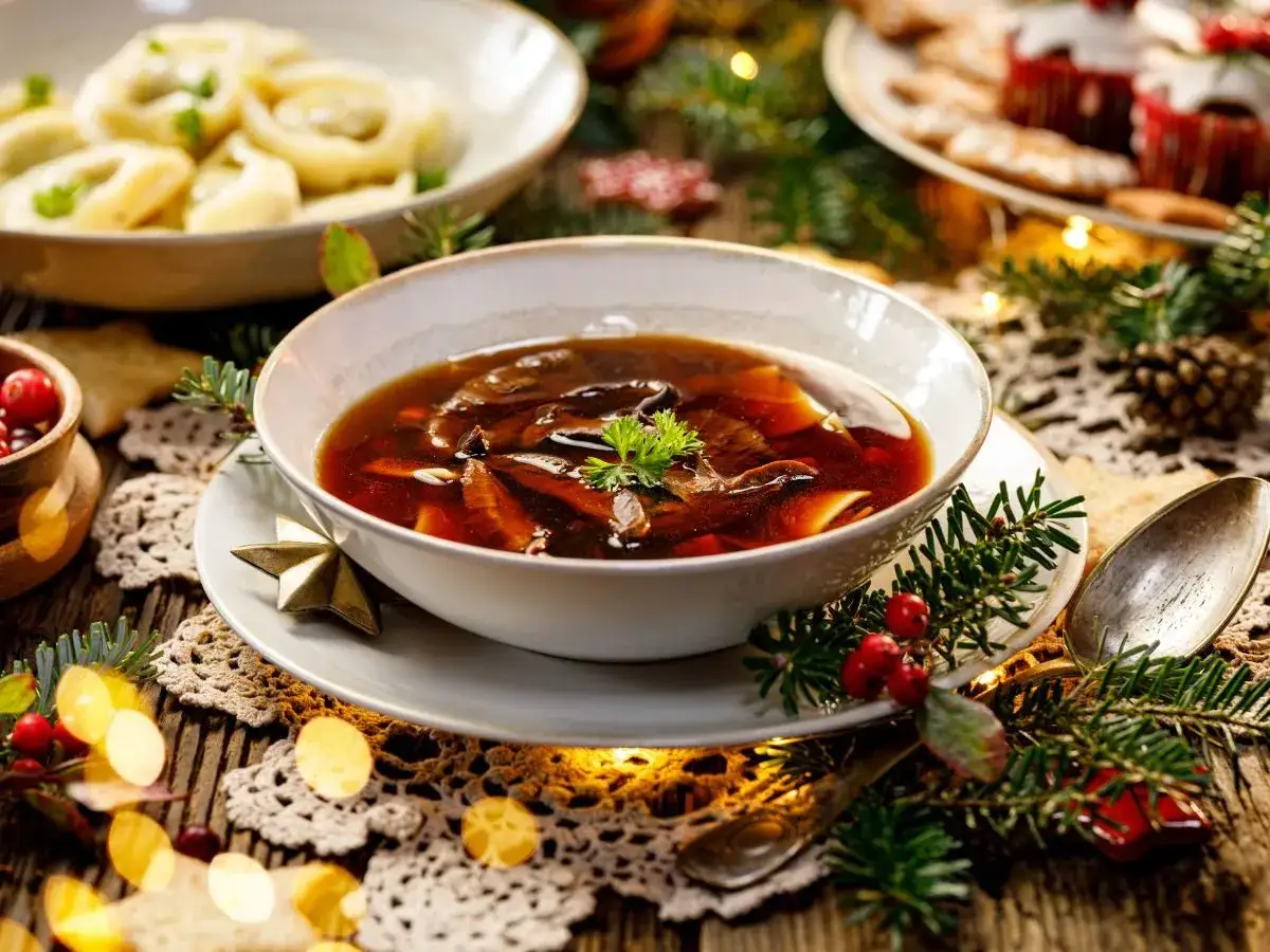 Aromatic zupa grzybowa z dodatkiem ziół, idealna na Wigilię. Obok pierogi i świąteczne dekoracje.