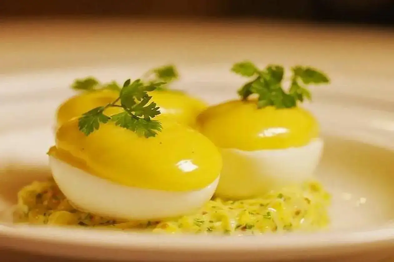 Trois moiti&eacute;s d'oeuf mayonnaise, garnies de persil frais, reposent sur une sauce cr&eacute;meuse.