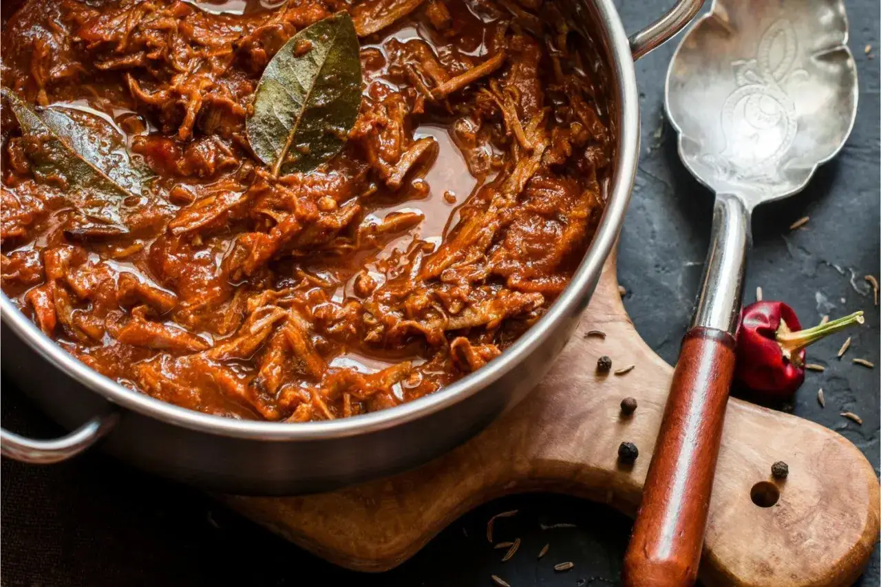 En gryta med mustig pulled beef i en smakrik sås, toppad med lagerblad. En sked och en liten röd chili ligger bredvid.