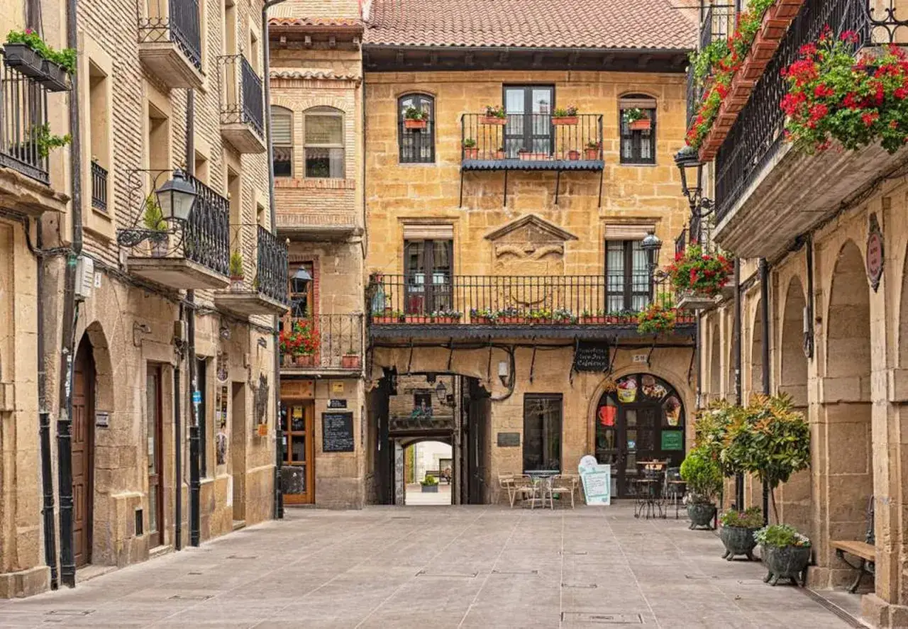 Calle empedrada con edificios de piedra dorada y balcones floridos. Un lugar perfecto para pensar **donde ir en el puente de diciembre**.