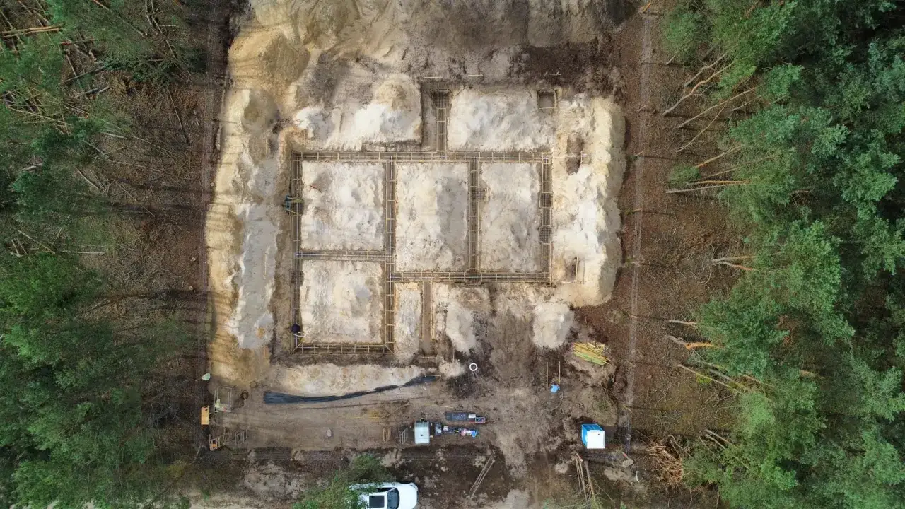 Budowa fundamentów domu w lesie. Widać zbrojenie i szalunki. Trwają badania geotechniczne gruntu.