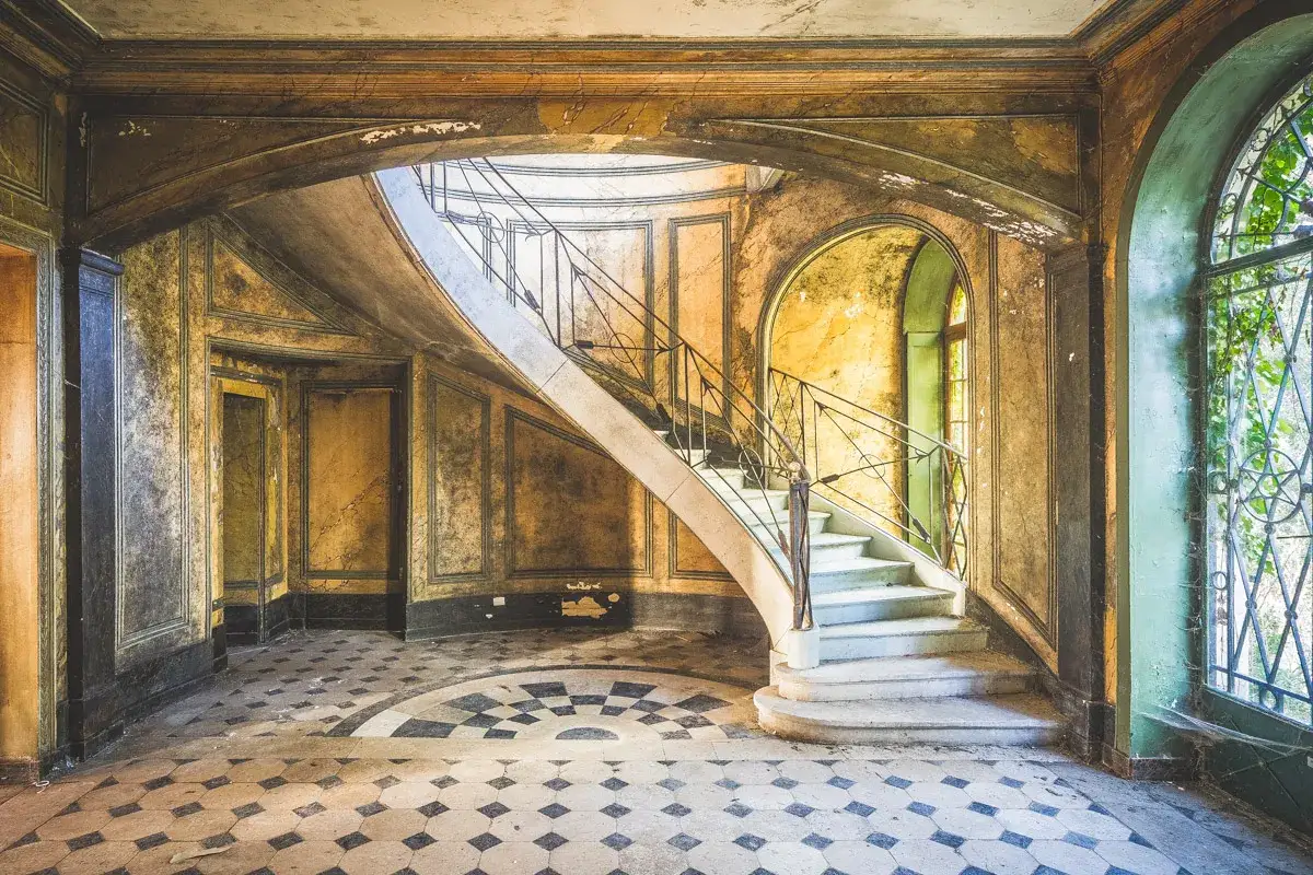 Escalier en colima&ccedil;on d'un manoir urbex abandonn&eacute;, aux murs d&eacute;cr&eacute;pits et au sol en mosa&iuml;que.