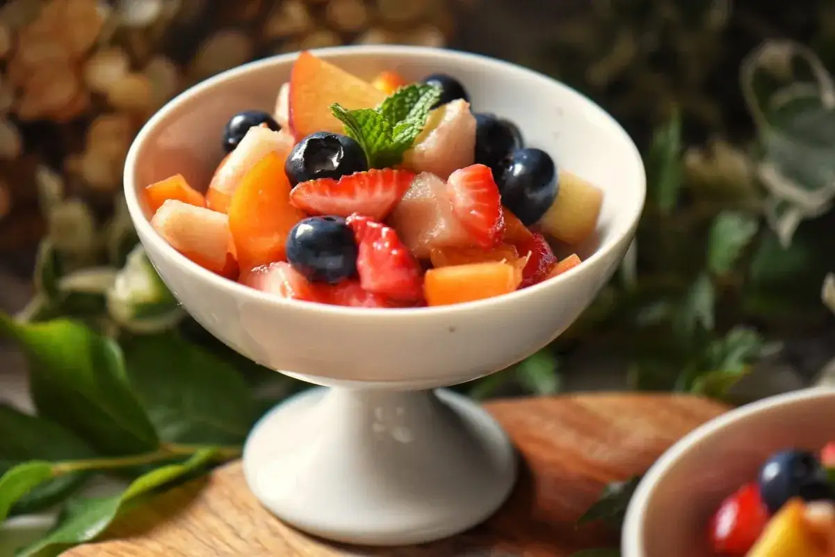Sch&uuml;ssel mit frischem, gekochtem Obst: Erdbeeren, Blaubeeren, Pfirsiche und Melone, garniert mit Minze.