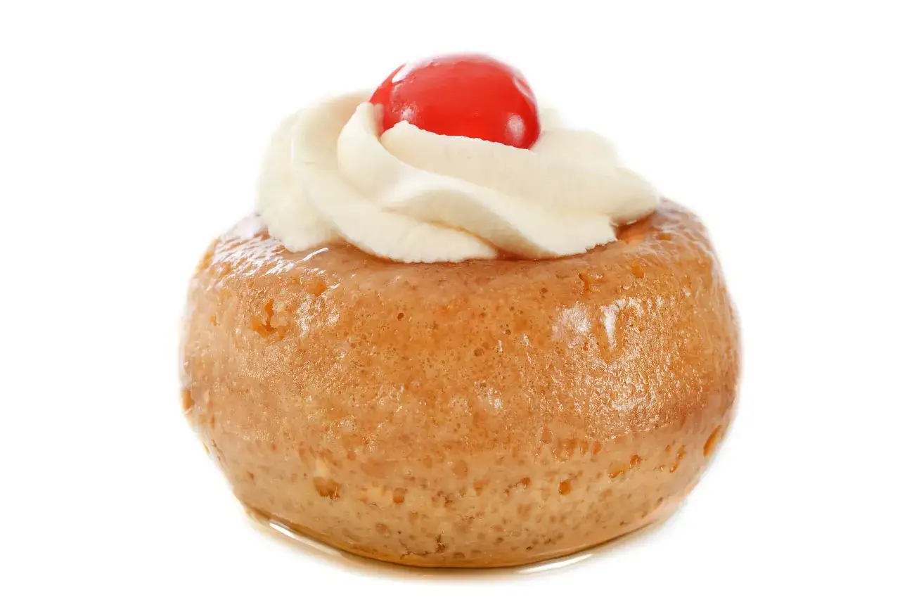 Un délicieux baba au rhum, moelleux et imbibé, surmonté de crème fouettée et d'une cerise rouge.