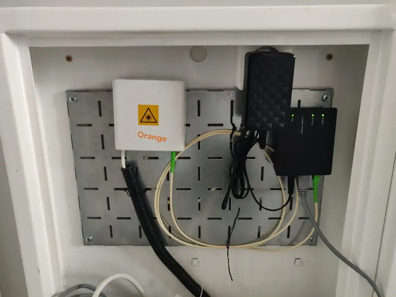 Urządzenie ONT od Orange z zielonymi i szarymi kablami, zasilaczem i wskaźnikami LED.