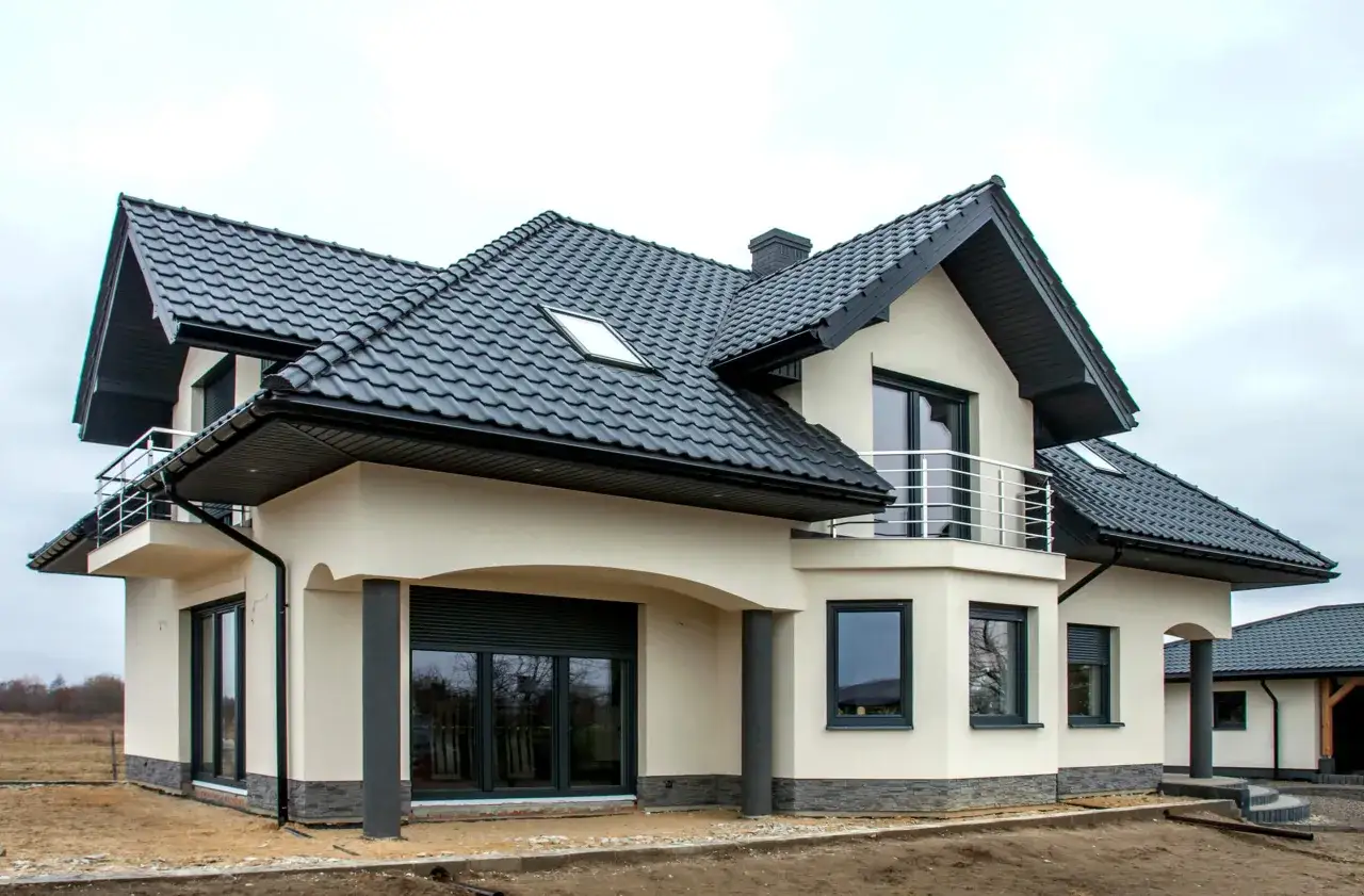 Nowy dom z jasnym tynkiem silikatowo silikonowym, czarnym dachem i balkonem.