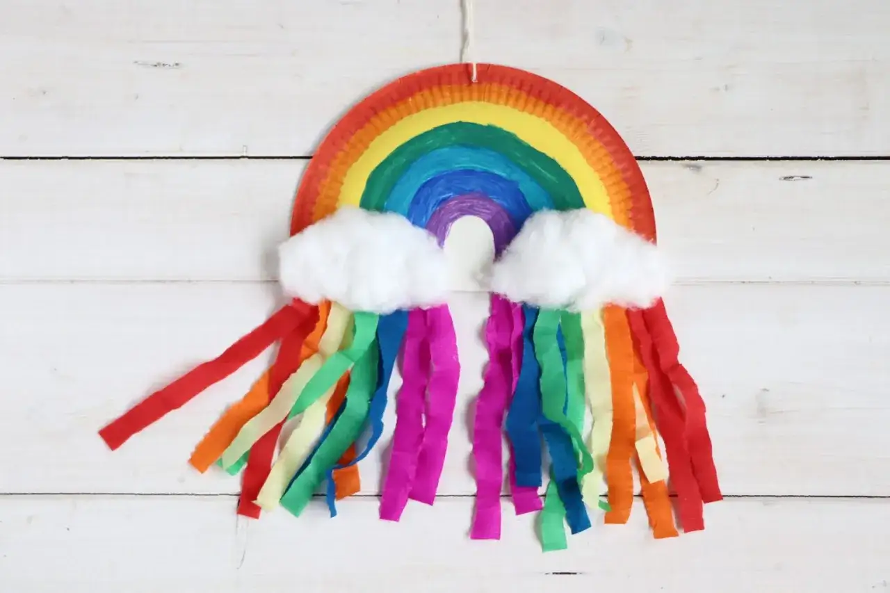 Ein selbstgebastelter Regenbogen mit bunten Papierstreifen und Watteb&auml;uschen als Wolken. Perfekt zum **Regenbogen basteln** f&uuml;r Kinder.