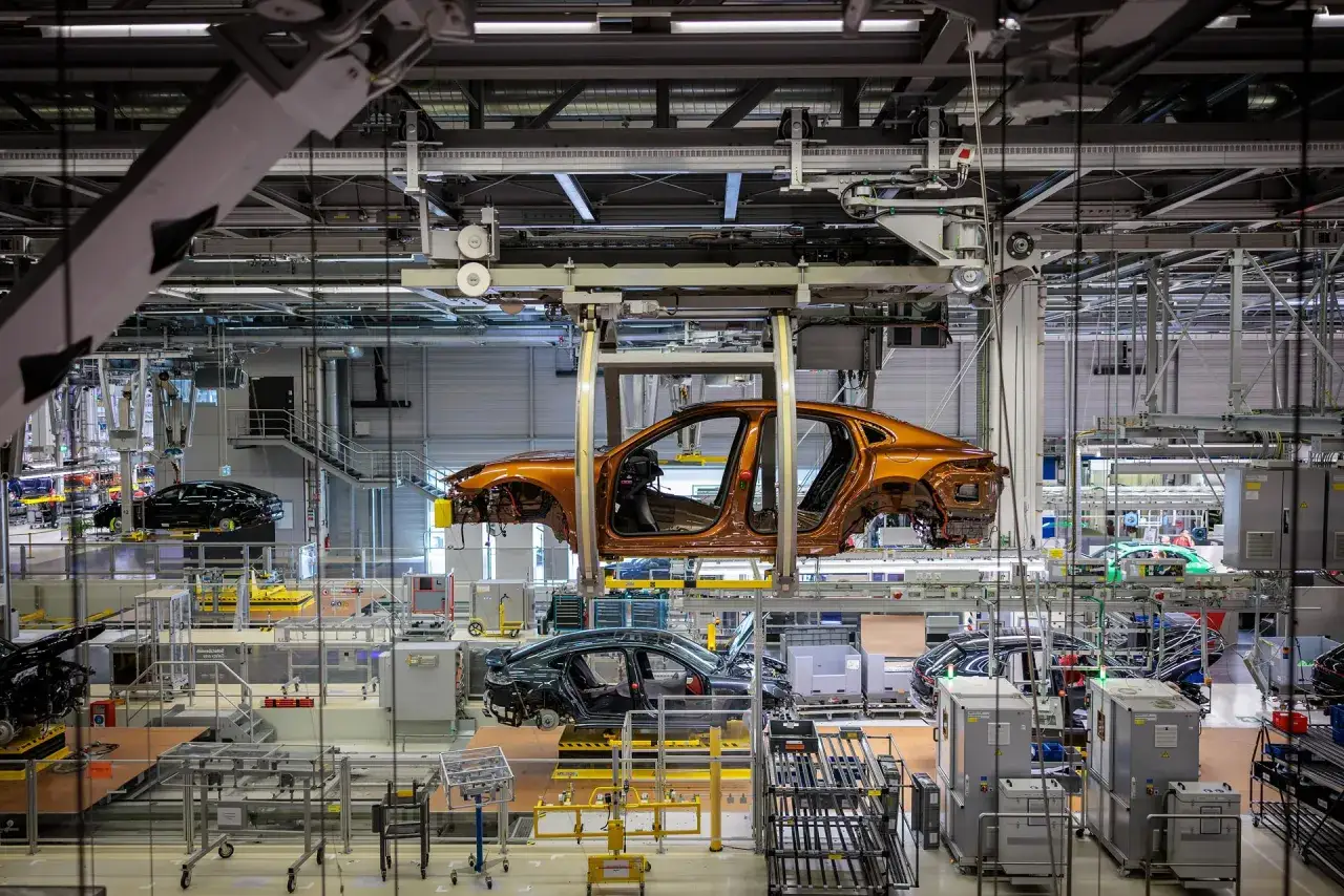 Linia produkcyjna, gdzie powstają samochody. Widoczny pomarańczowy karoseria Porsche, który jest montowany. To właśnie tutaj Porsche produkuje swoje luksusowe auta.