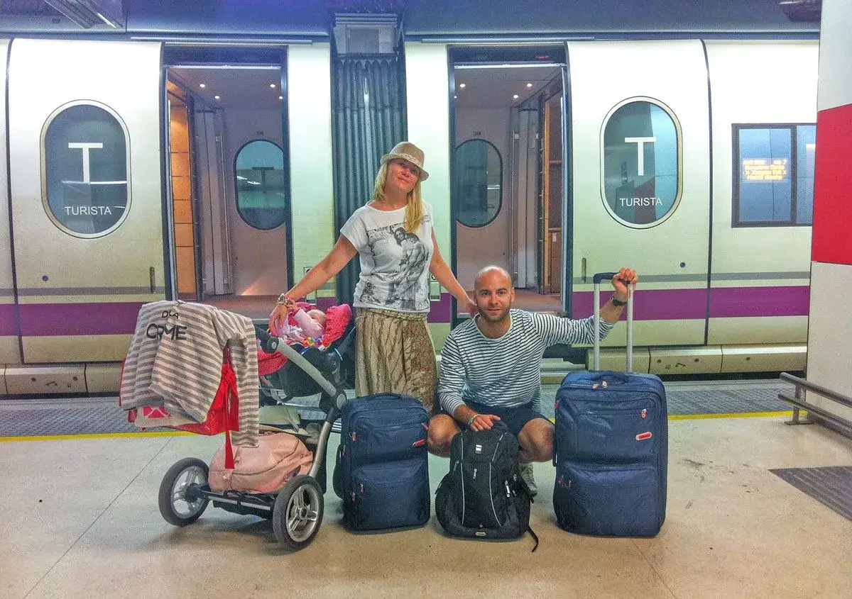 Familia lista para su viaje en tren por España. Equipaje, carrito de bebé y sonrisas en el andén.