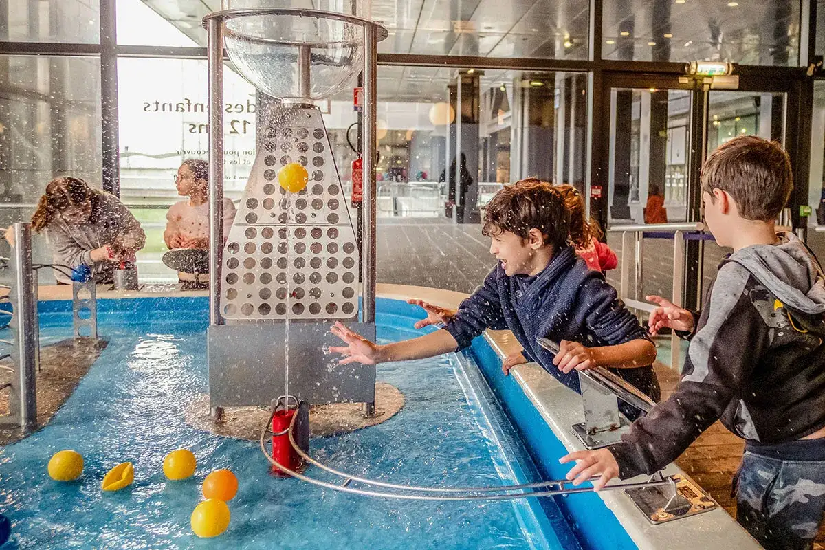 Des enfants s'amusent avec une cascade interactive dans un musée de science à Paris. L'eau éclabousse joyeusement.