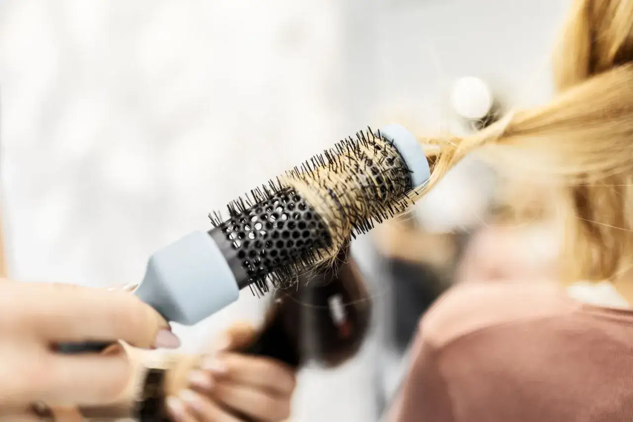 Profesjonalny blowout blond włosów z użyciem okrągłej szczotki i suszarki.