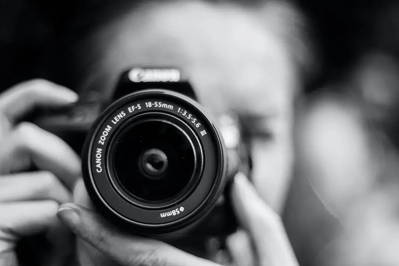 Zbliżenie na obiektyw aparatu Canon, trzymanego przez fotografa. Profesjonalne usługi fotograficzne, rozliczane z VAT.