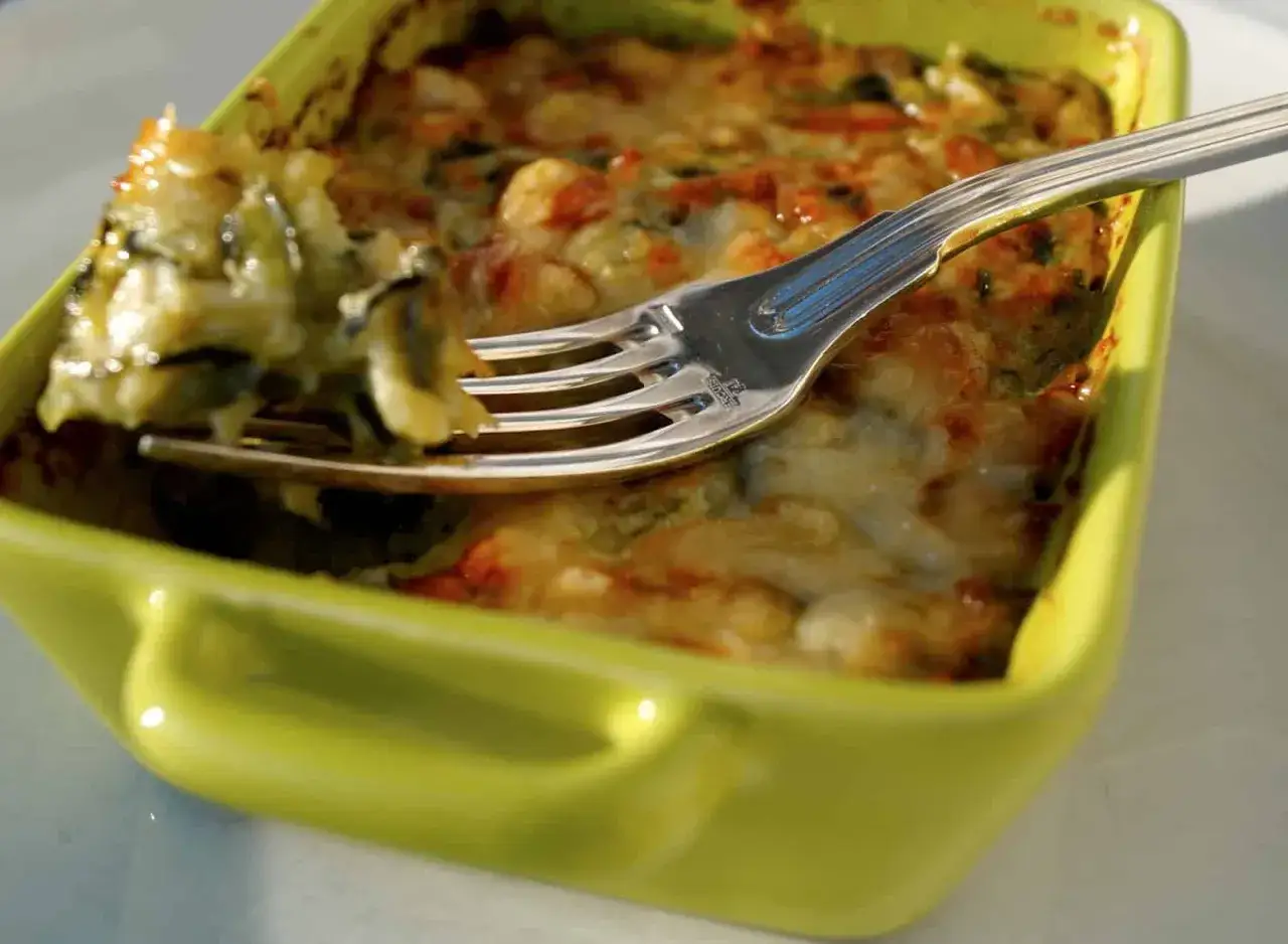 Une fourchette pr&eacute;l&egrave;ve une bouch&eacute;e d'un gratin de courgettes cr&eacute;meux et gratin&eacute;, servi dans un plat vert vif.