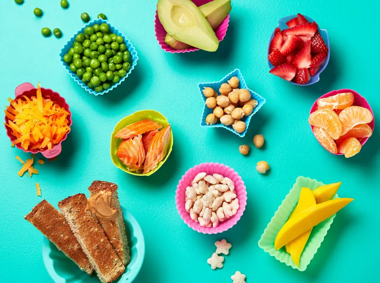 Bunte Sch&auml;lchen mit gesunden Lebensmitteln wie Erbsen, Erdbeeren, Mango, Lachs und Toast mit Erdnussbutter &ndash; tolle Ideen f&uuml;r Babybrei Rezepte ab 8. Monat.