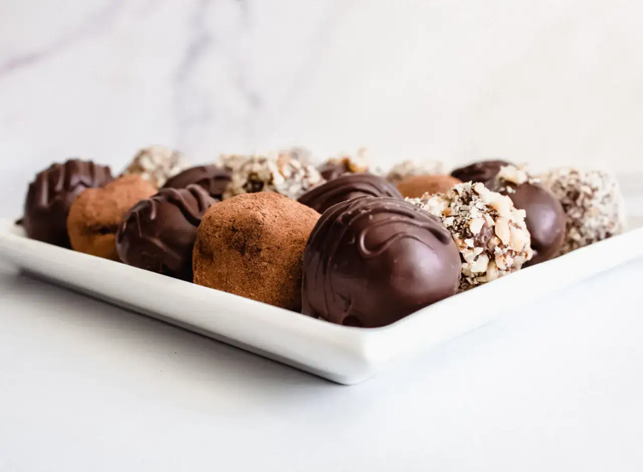 Variedad de trufas de chocolate, algunas cubiertas de cacao en polvo, otras con chocolate derretido y trozos de frutos secos.
