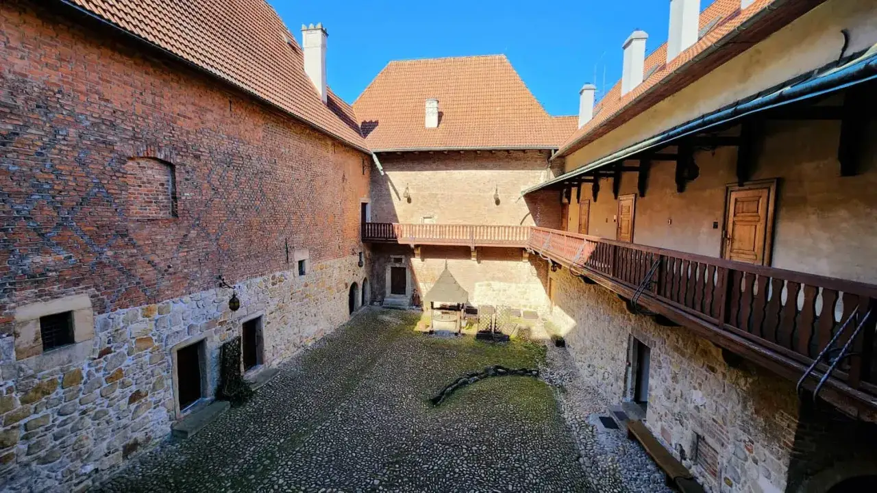 Dziedziniec zamku w Dębnie z kamienną posadzką, drewnianymi gankami i ceglanymi murami.
