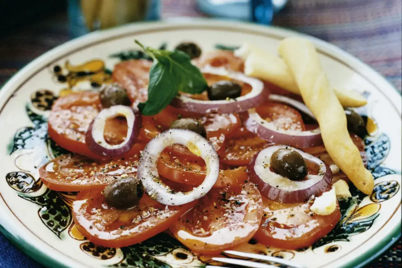 En l&auml;cker italiensk potatissallad med tomater, r&ouml;dl&ouml;k, oliver och basilika, serverad med grissini.