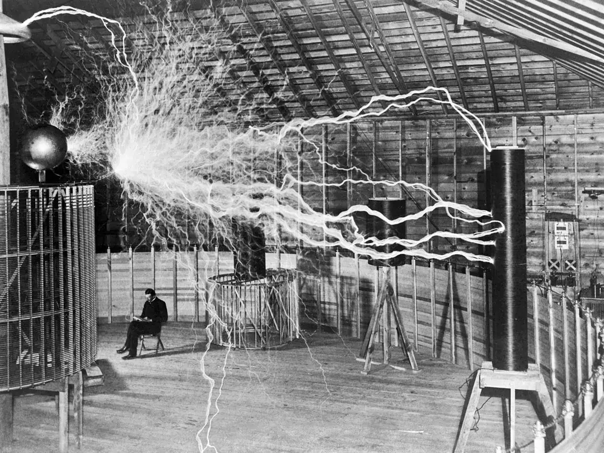 Nikola Tesla, który wynalazł prąd, siedzi spokojnie wśród wyładowań elektrycznych w swojej pracowni.