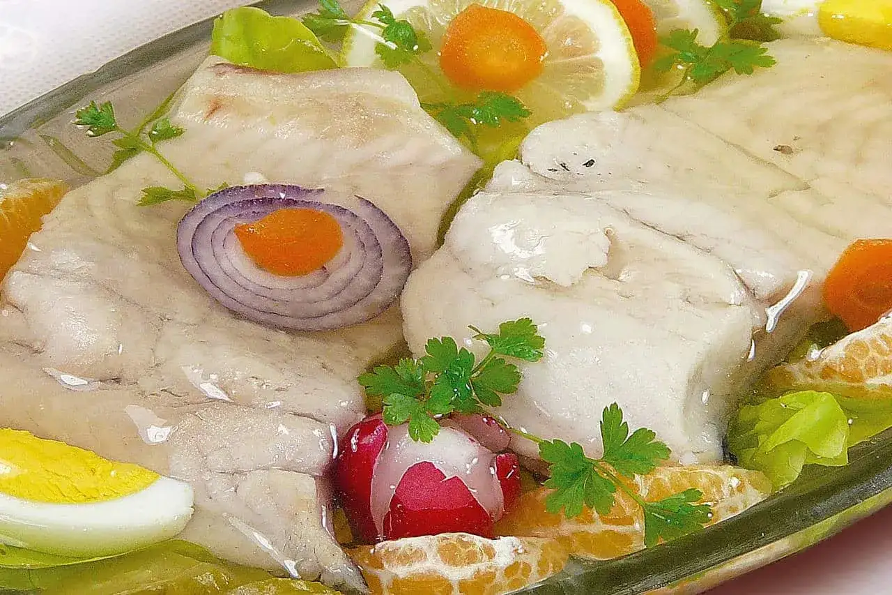 Filet z karpia w galarecie, ozdobiony plasterkami cytryny, pomarańczy, jajka i cebuli.