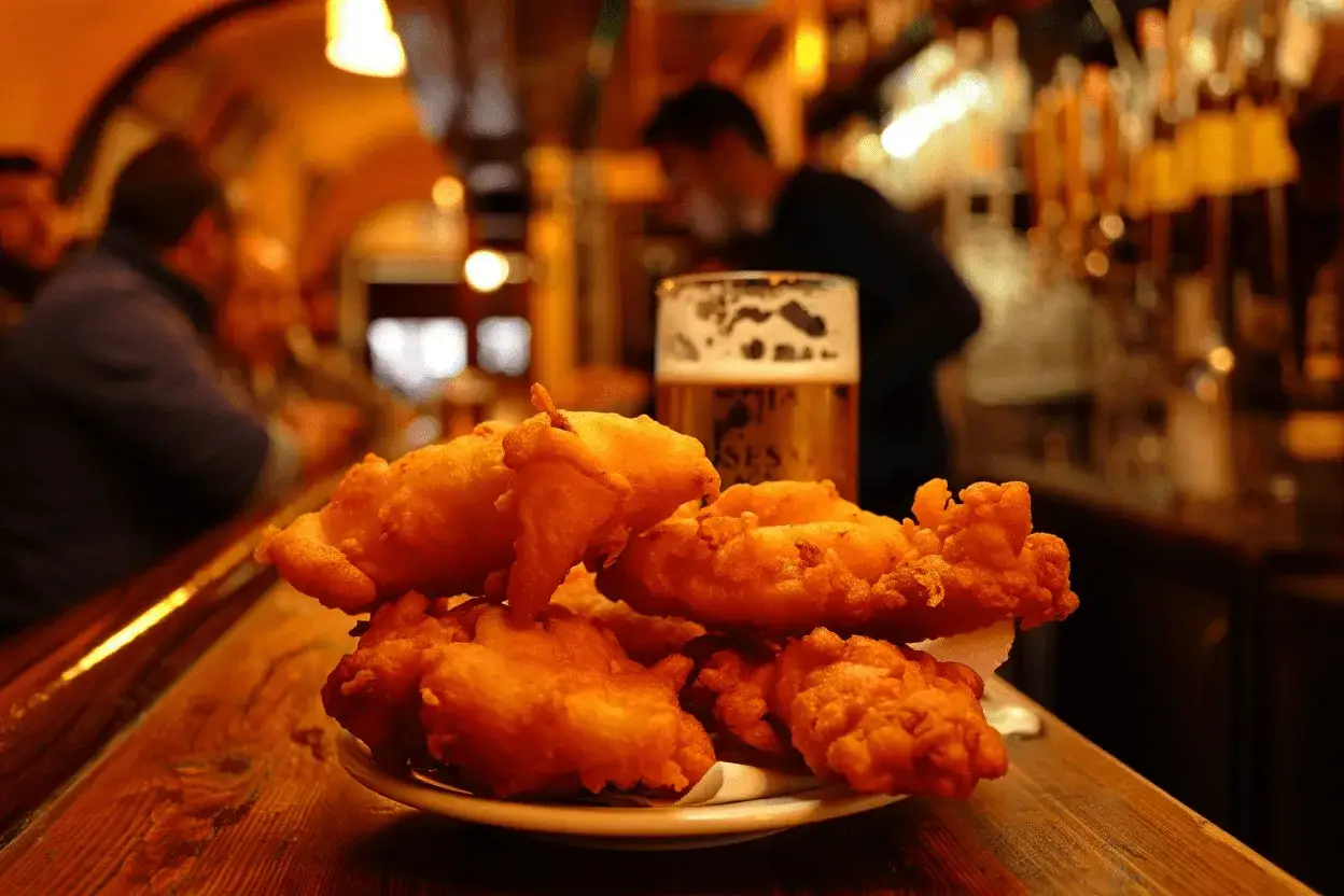 Un plato de bacalao rebozado dorado y crujiente, acompañado de una cerveza espumosa en un bar acogedor.