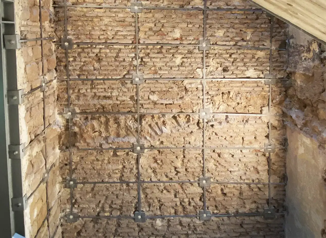 Muro in mattoni con rinforzi metallici a griglia, parte di un **intervento locale** di consolidamento.