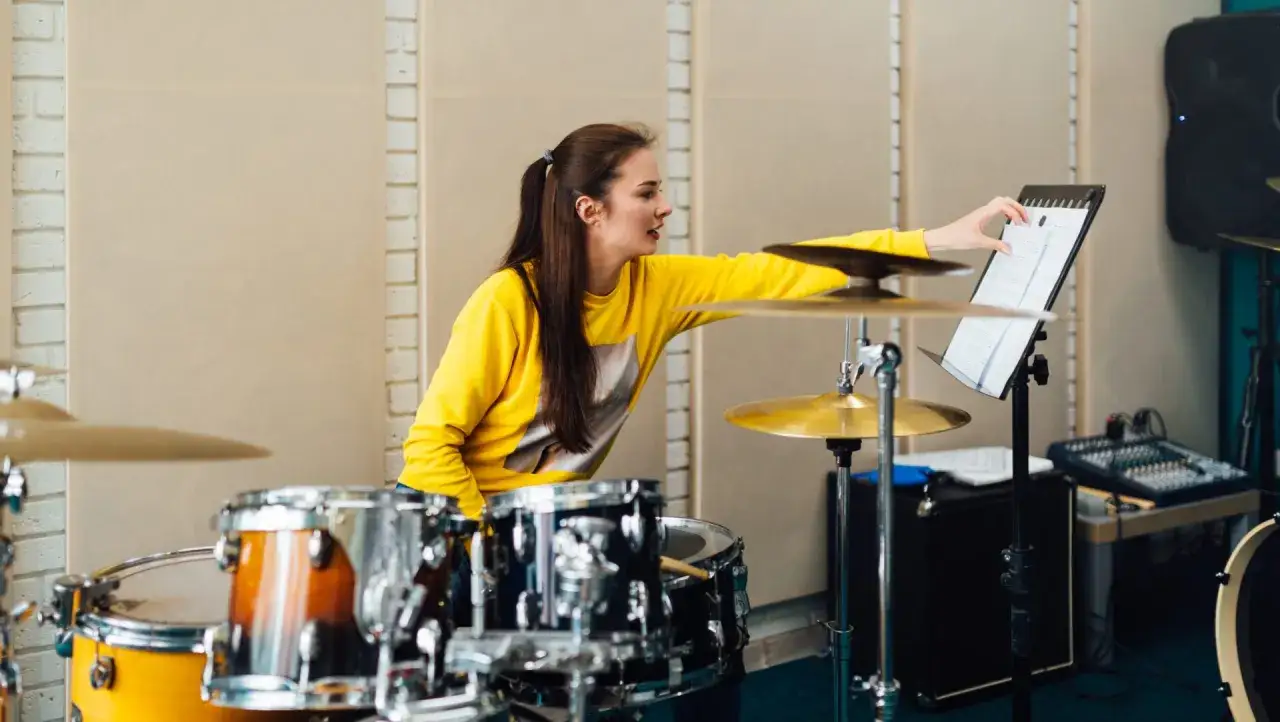 Jeune batteuse en sweat jaune, concentrée sur sa partition, prête à trouver le bon groove musique.